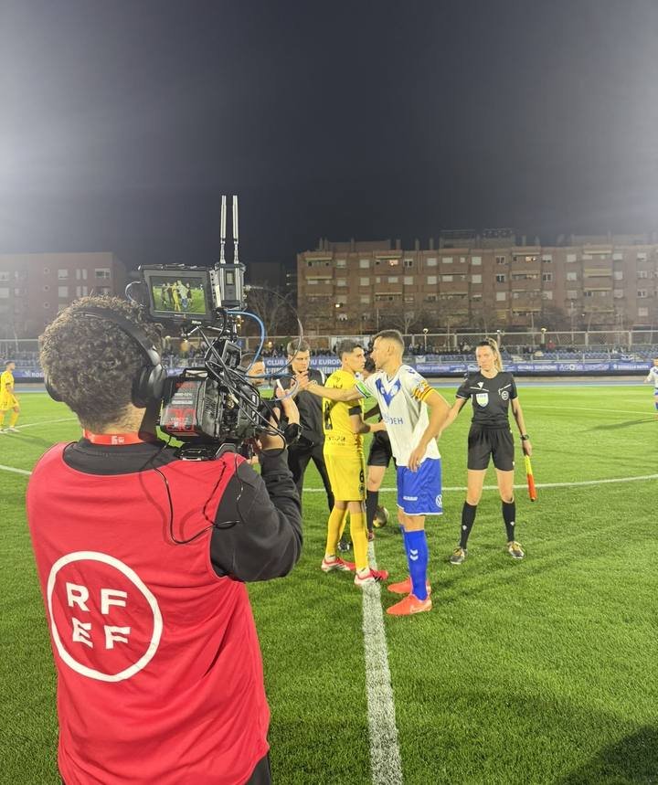 Operador de cámara con peto de la RFEF grabando a los equipos antes de un partido nocturno