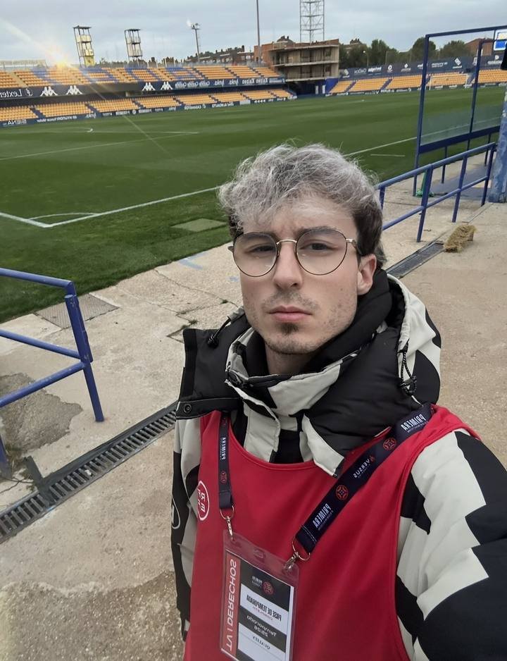 Diego en la banda de un estadio, con peto y acreditación